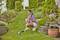 A person in summer clothing is trimming the lawn with a lawnmower in a well-maintained garden with flowers and bushes.