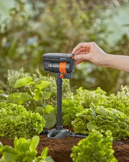 A hand adjusts a garden irrigation timer among lush green plants in a garden, illustrating automated watering control.