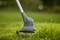 A lawn trimmer precisely trims green grass in a garden. The focus is on the cutting head in close-up.