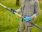 A person outdoors is holding a telescopic tube, wearing blue gloves and casual clothing. In the background is a green meadow.