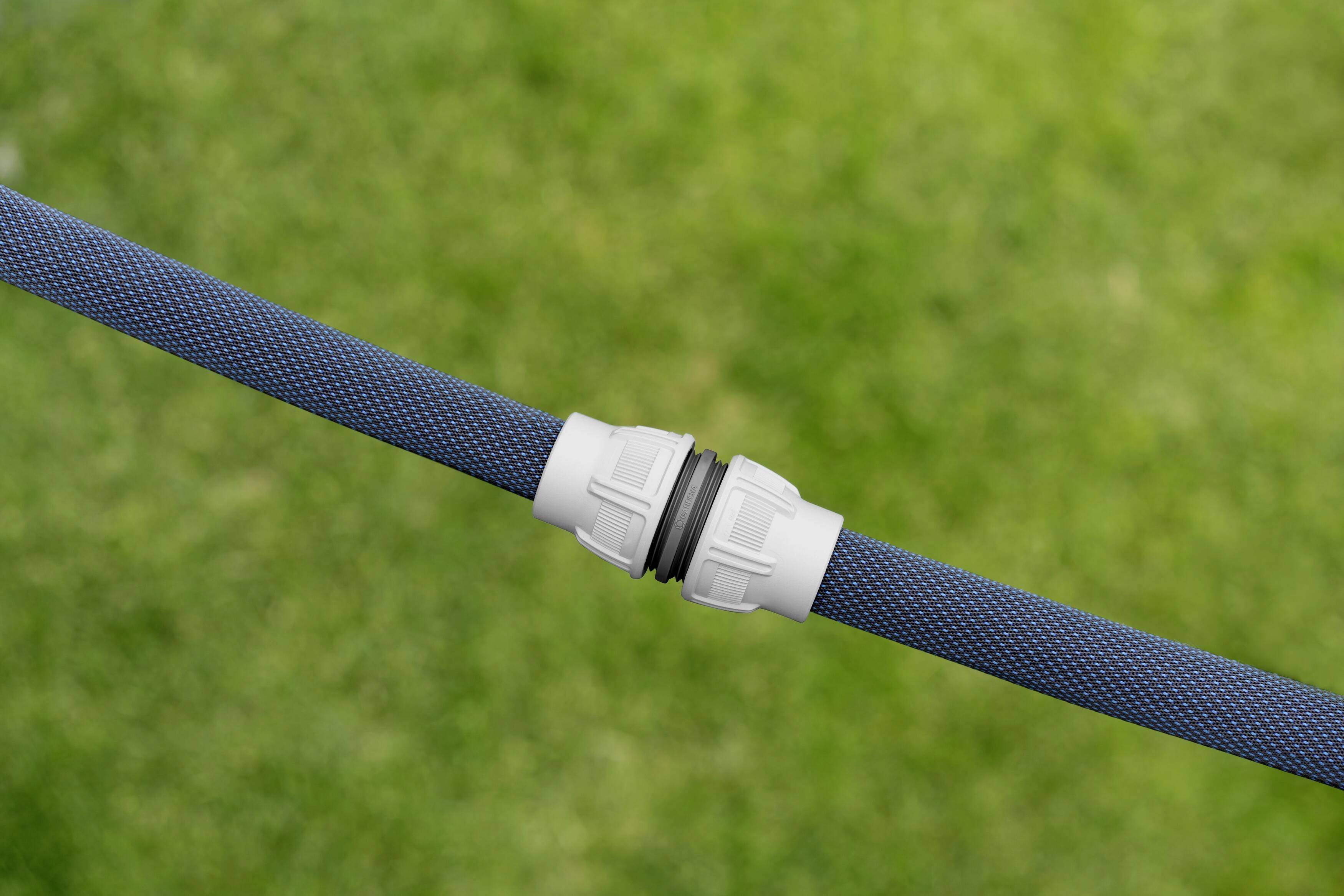 A dark blue hose is connected with a white fitting on green grass.
