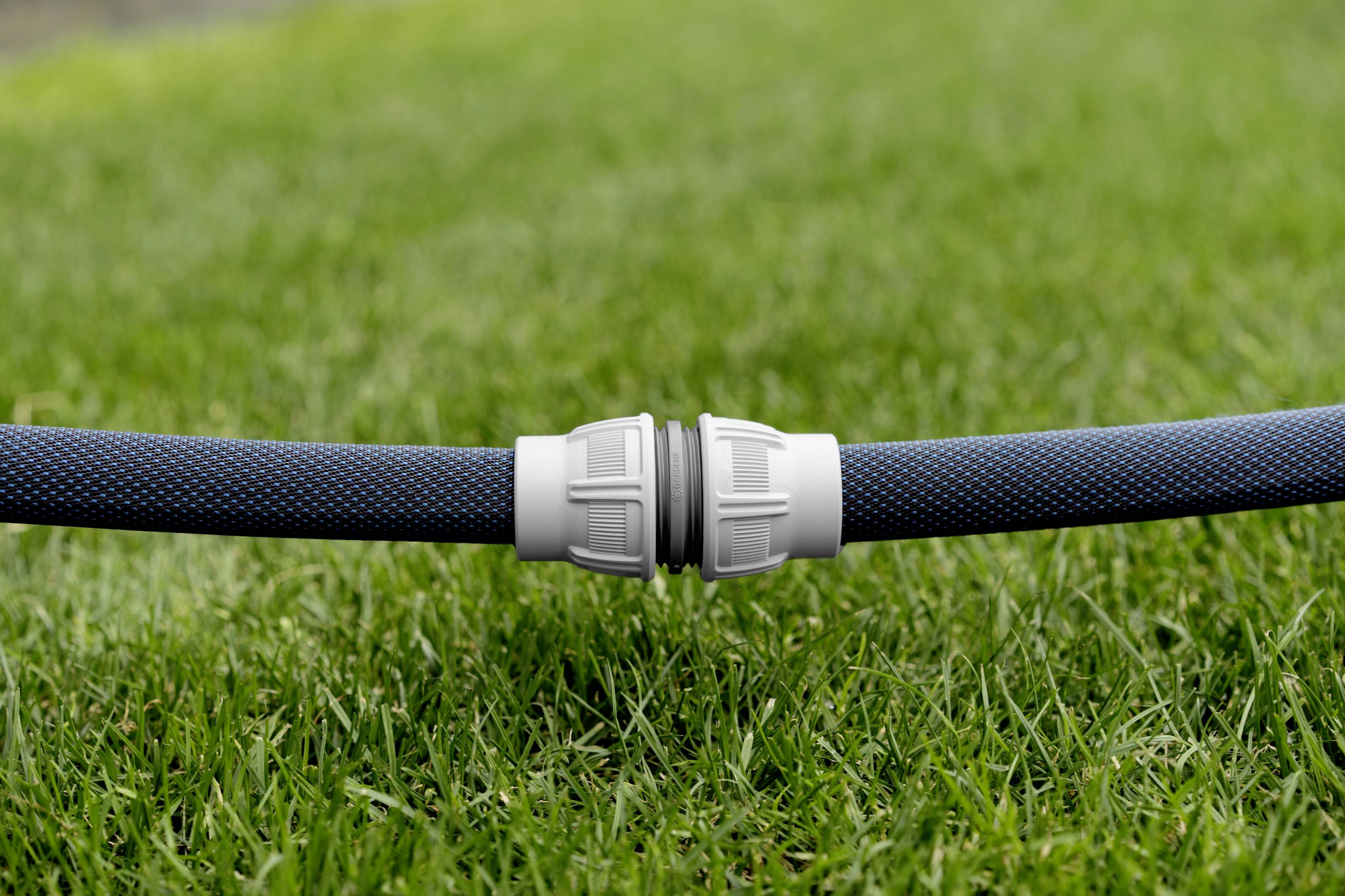 A garden hose lies on green grass, connected by a white plastic coupling.