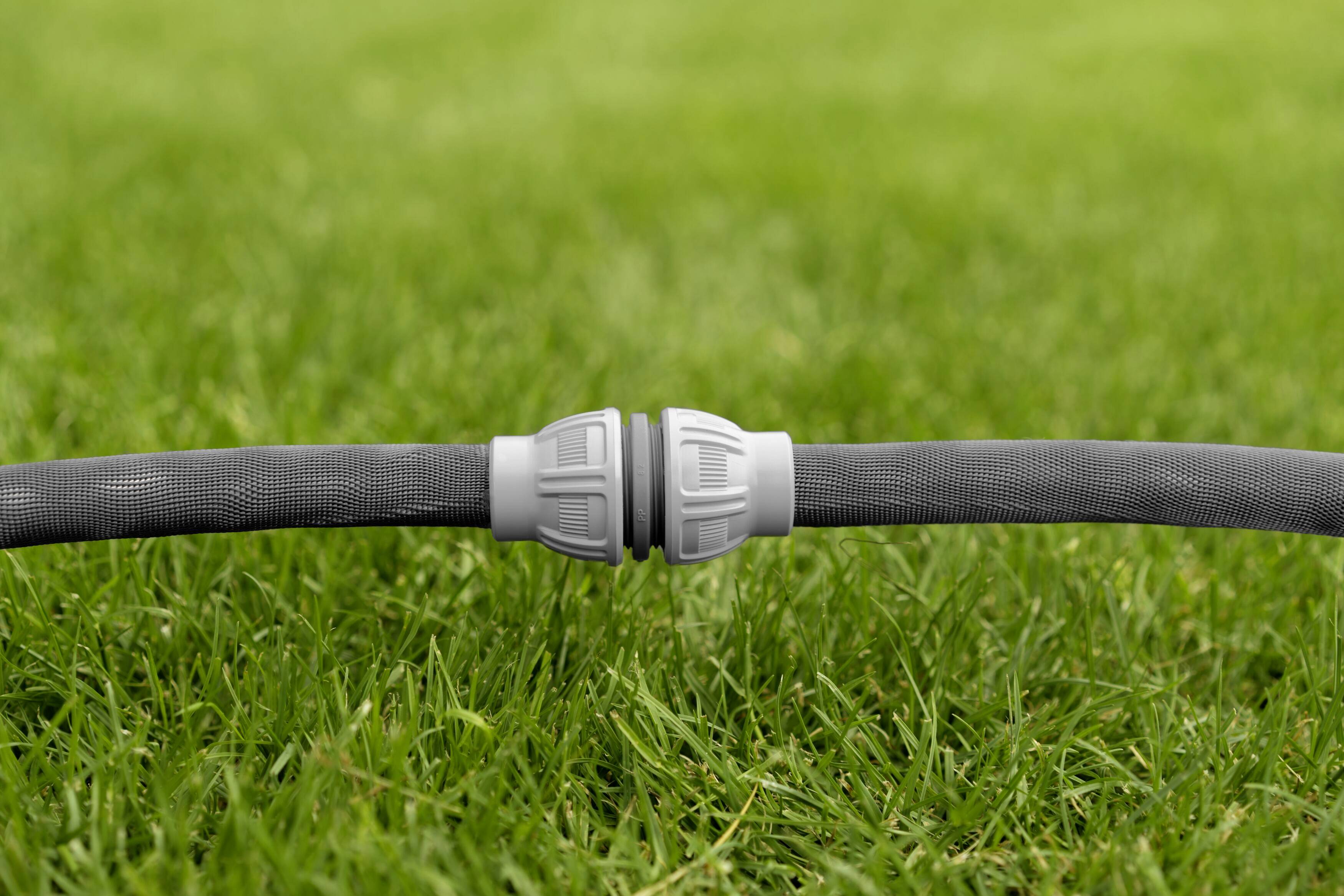 Grey garden hose on green grass, connected with a plastic coupling in the middle.