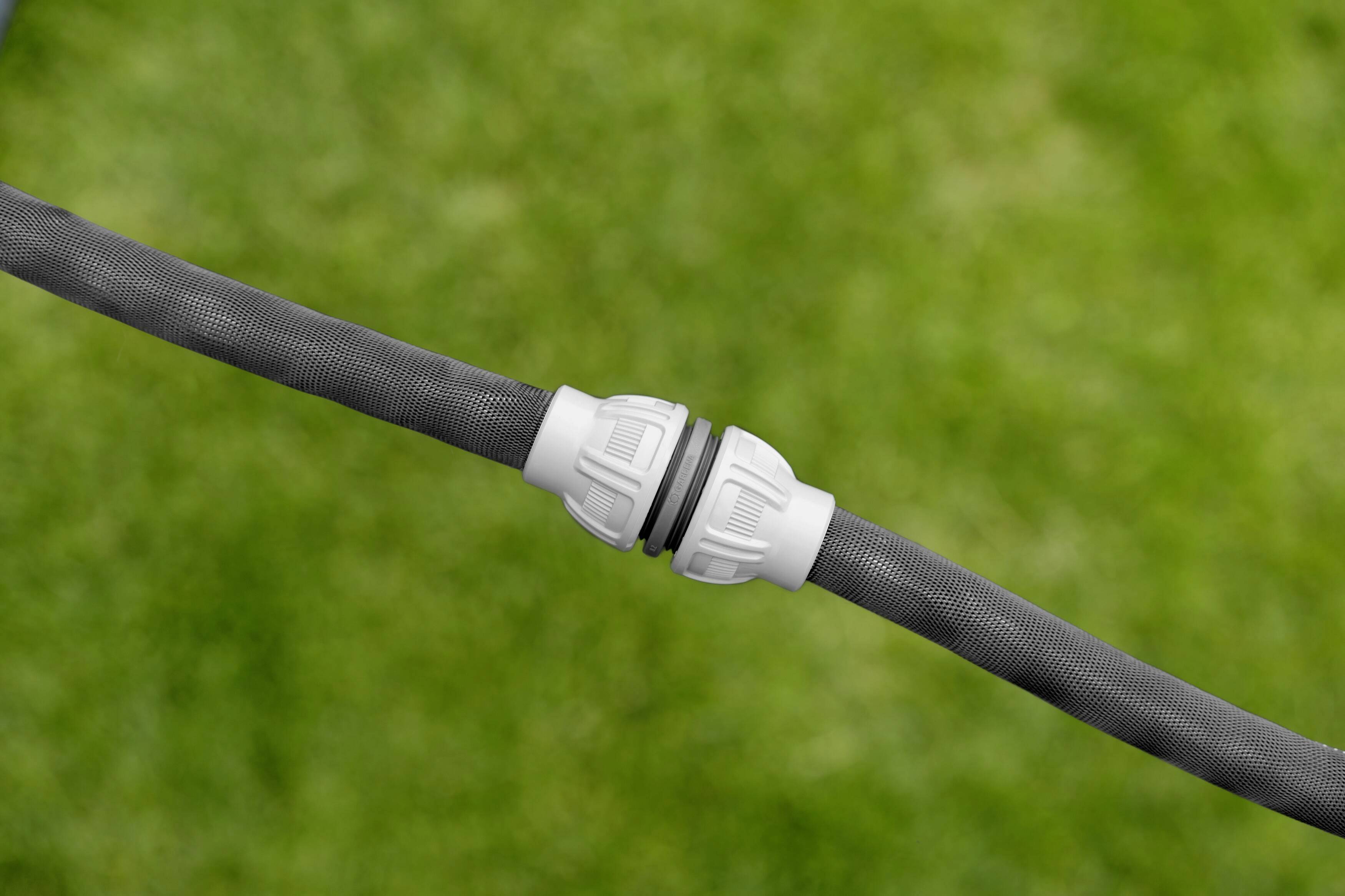 Two garden hoses are connected with a white coupling piece, with green lawn in the background.
