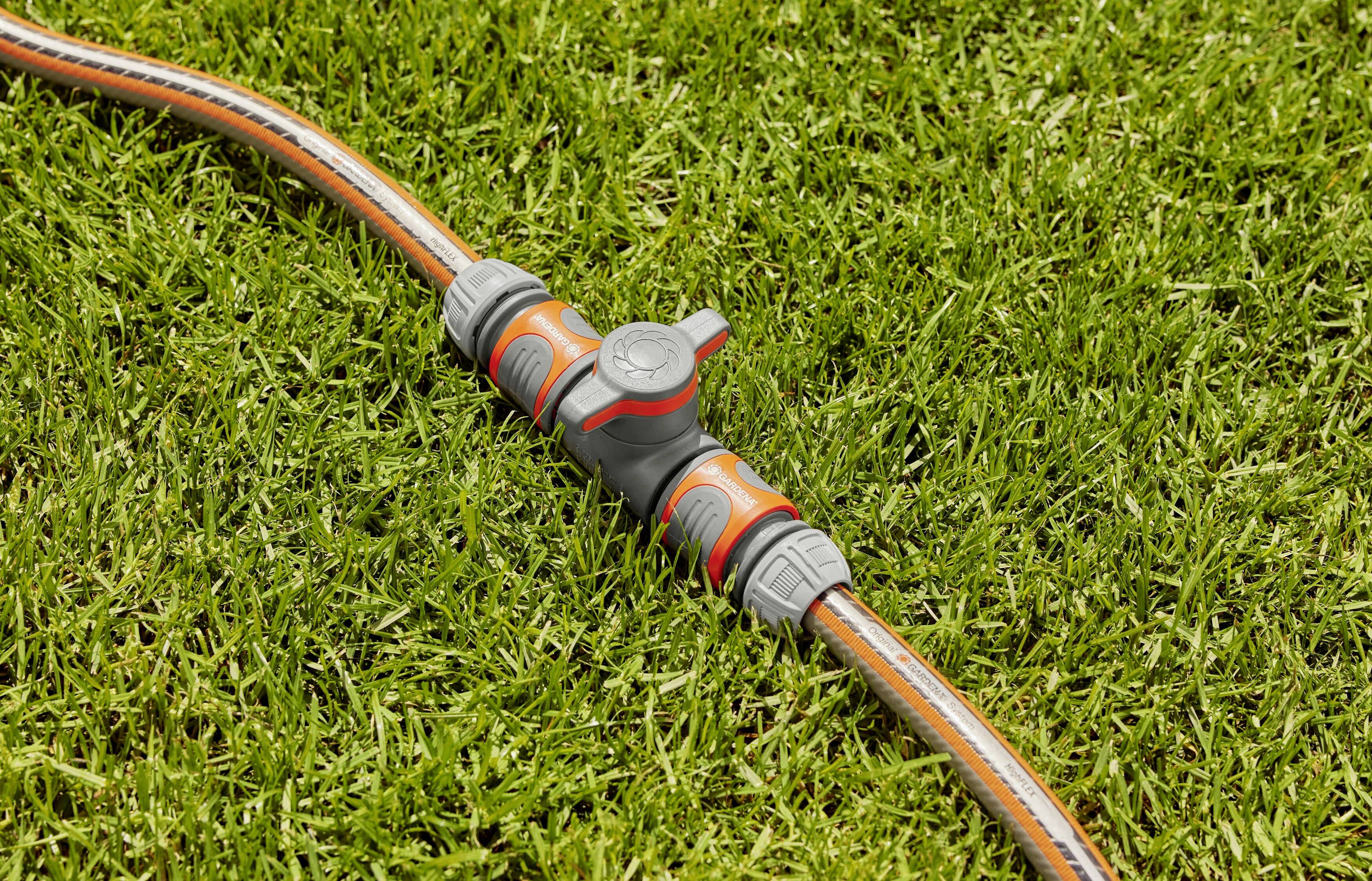 A hosepipe lies on green grass, connected through a grey, T-shaped valve.