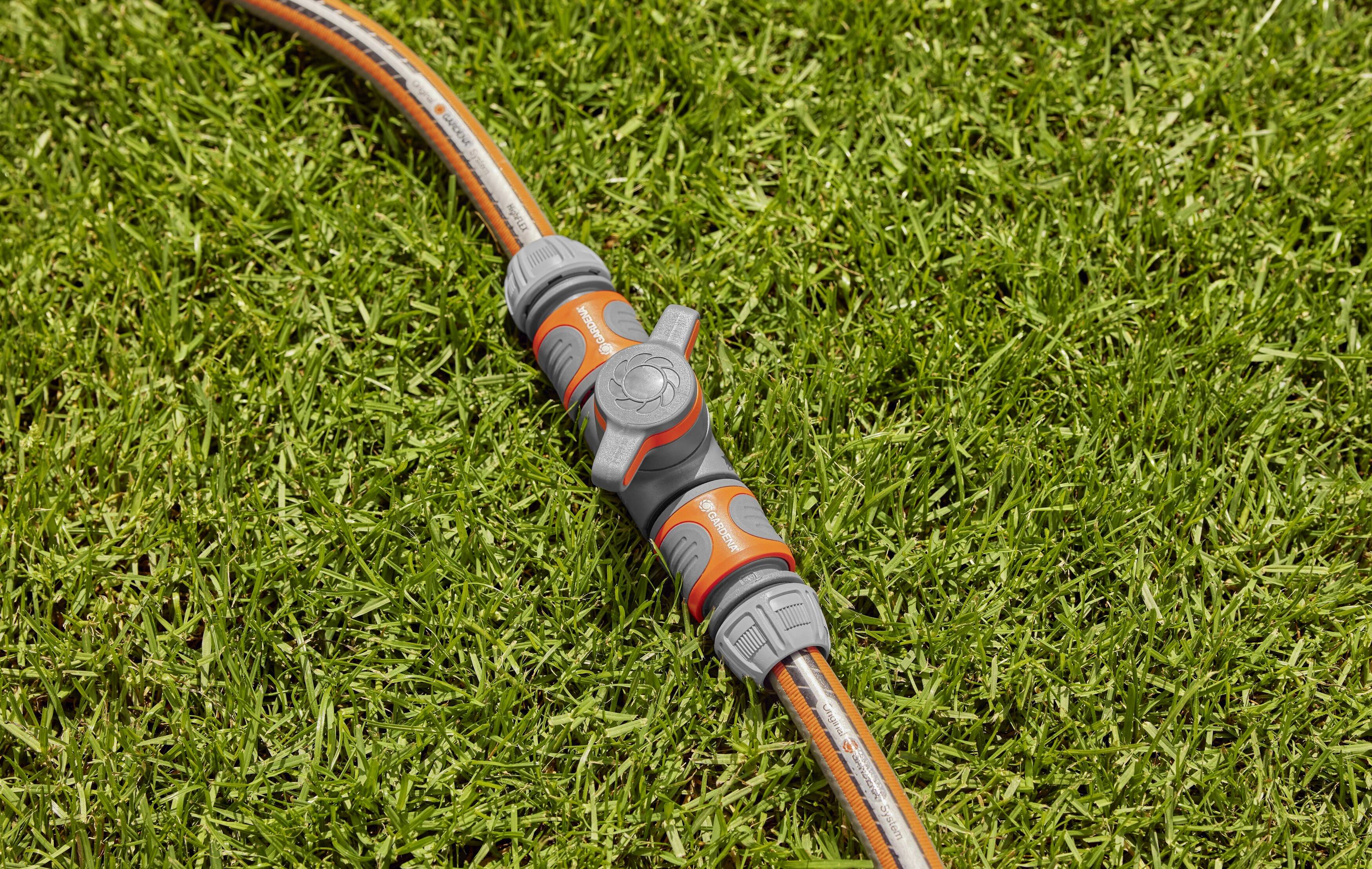 A garden hose with a connector lies on green grass. The connector is grey and orange and is used for water control.