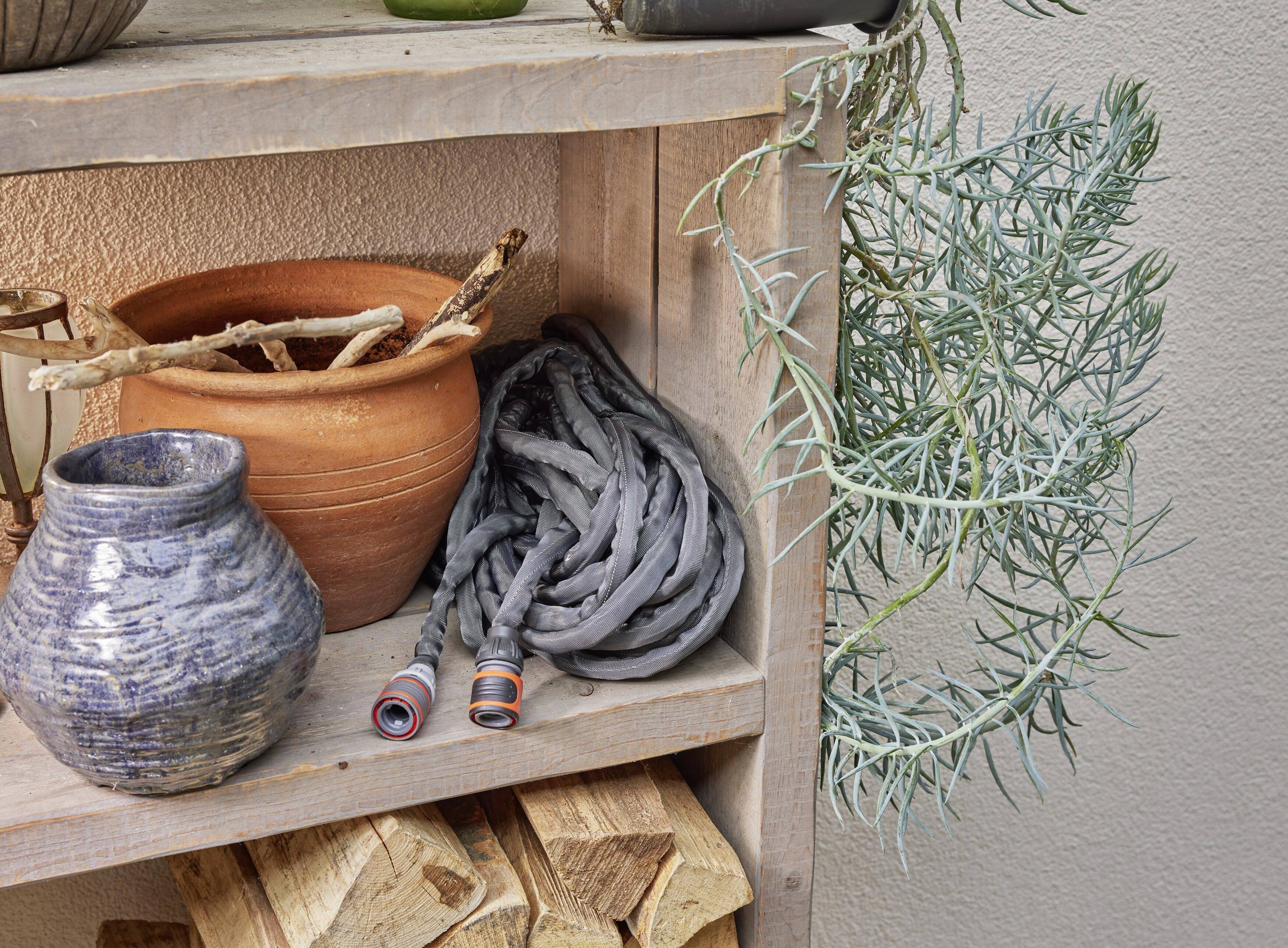 Shelf with clay pots, two coiled grey garden hoses and branches of a plant. Stacked firewood underneath.