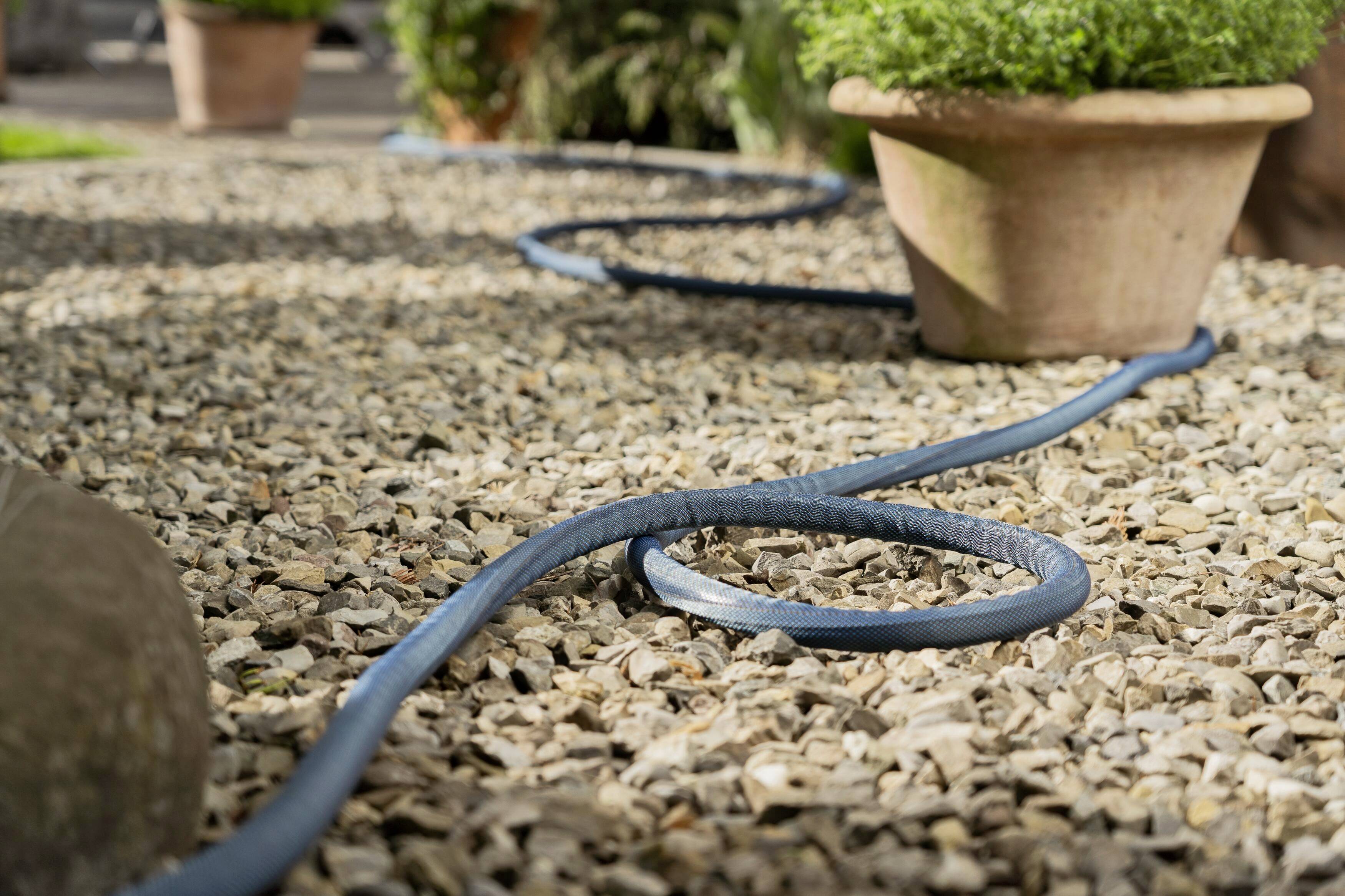 A hosepipe winds its way across a gravel path between two potted plants in the garden.