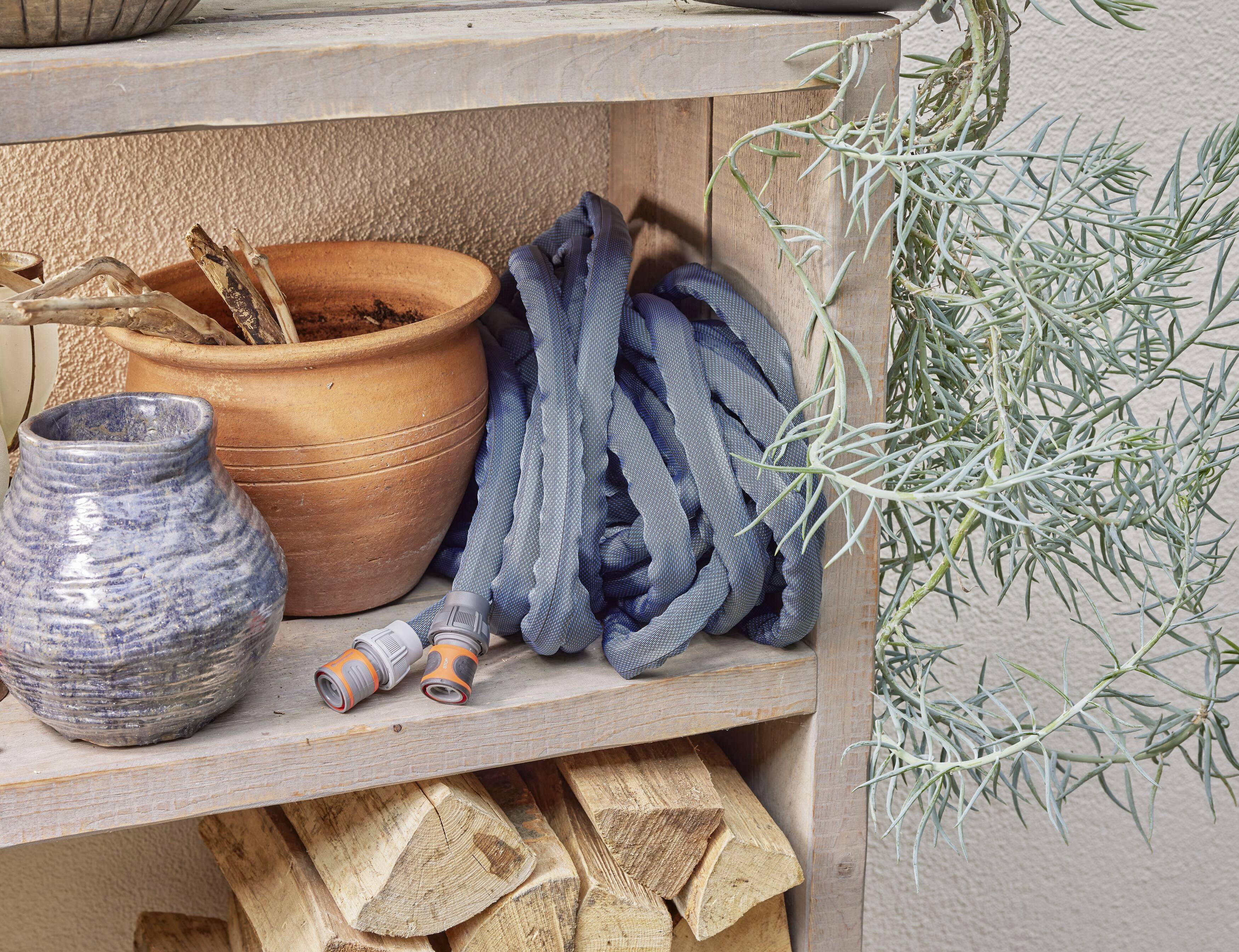 Potted plants and batteries are placed on a wooden shelf. A woven, grey object lies between the items.