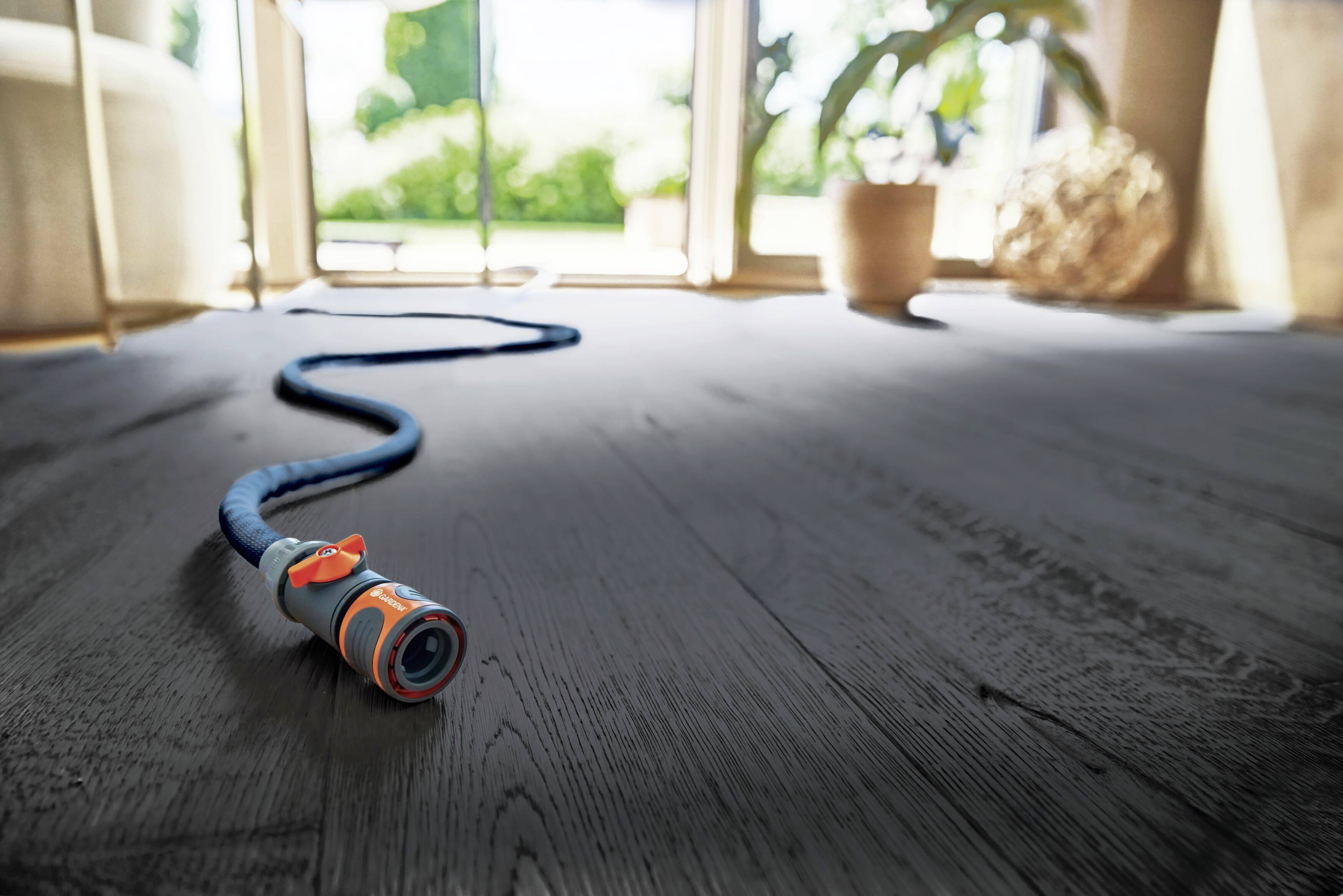 A garden hose lies on the floor in a bright room. Plants and an open window are visible in the background.