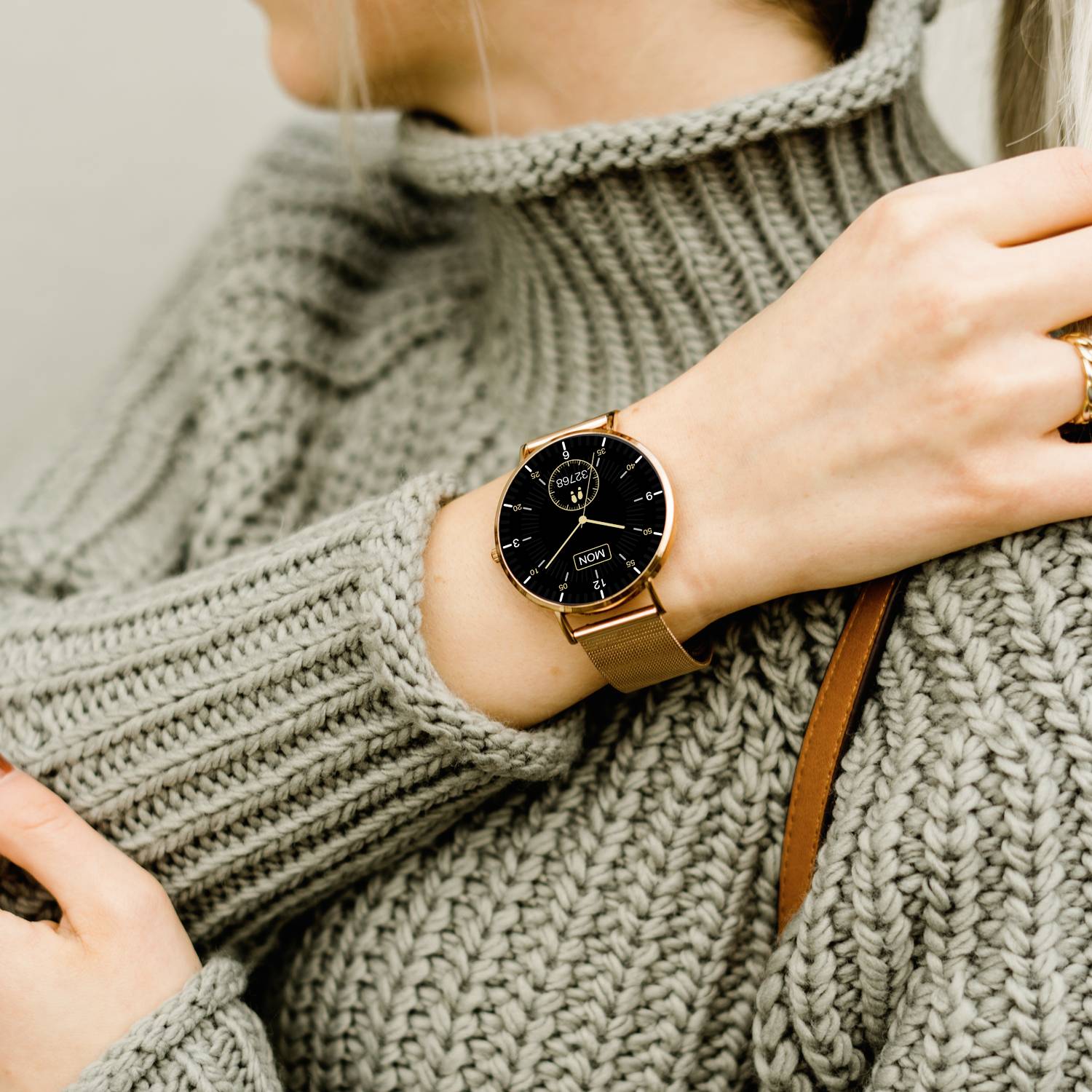 A person is wearing a grey knitted jumper and an elegant analogue wristwatch with a brown strap.