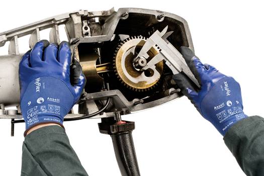 A mechanic wearing blue gloves is using a calliper to measure a gear in a metal machine.