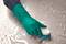 A hand wearing a green rubber glove holds a brush and scrubs a wet, soapy surface.