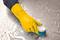 A hand wearing a yellow rubber glove is using a brush to clean a wet surface with soapy water.
