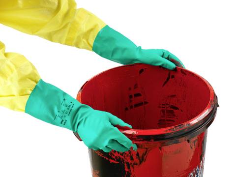 A person in a yellow protective suit and green gloves is holding a red bucket.