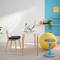 Modern workspace with a white desk, laptop, yellow exercise ball and blue stool in front of a turquoise wall.