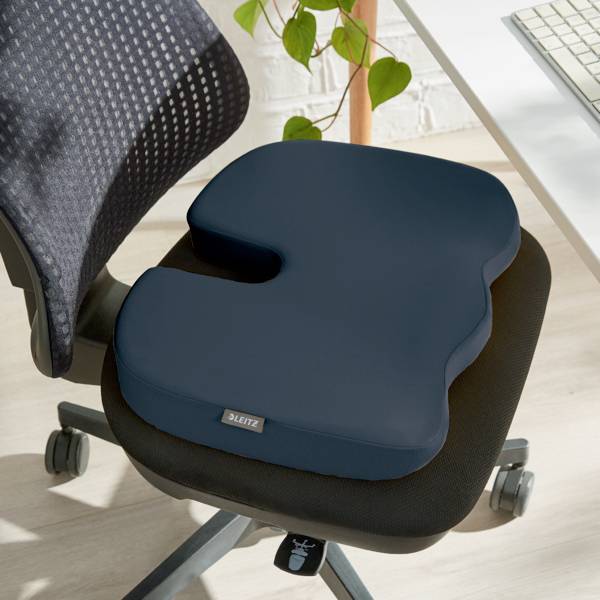 An ergonomic seat cushion on an office chair, next to a table with a green plant.