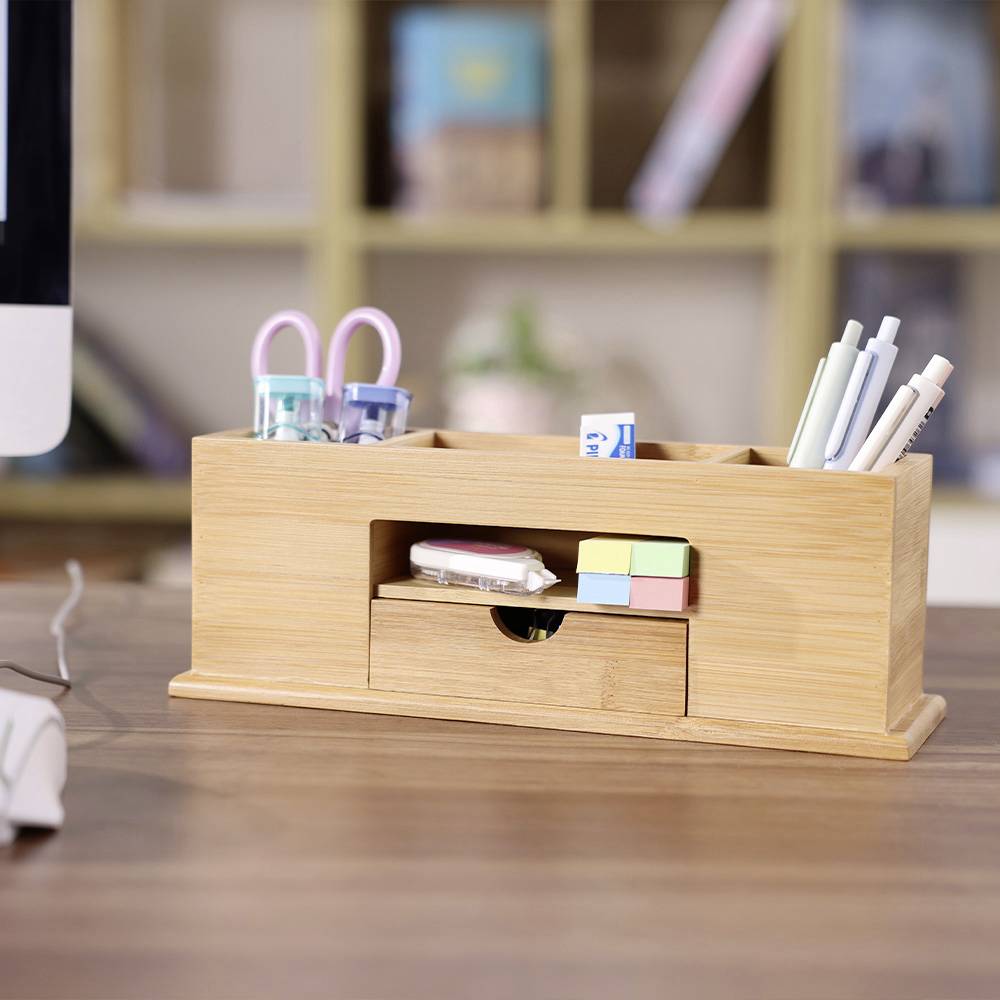 Wooden desk organiser with pens, scissors, and sticky notes, positioned on a desk next to a computer monitor.