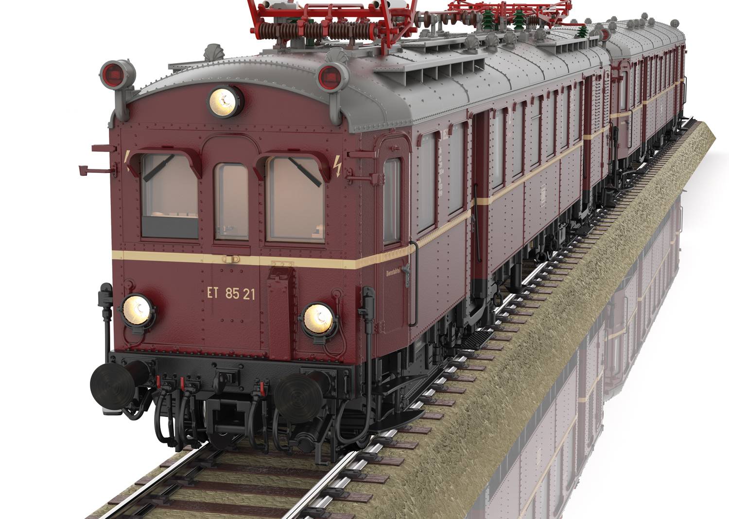 A red historical train travels on a track, viewed from the front. The train has round headlamps and is painted a dark red colour.