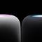 Two smart speakers with illuminated tops against a black background. The left light is colourful, the right one blue.