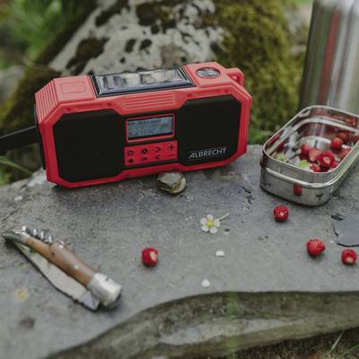 A red portable radio on a stone outdoors, beside it a penknife and a small tin of strawberries.
