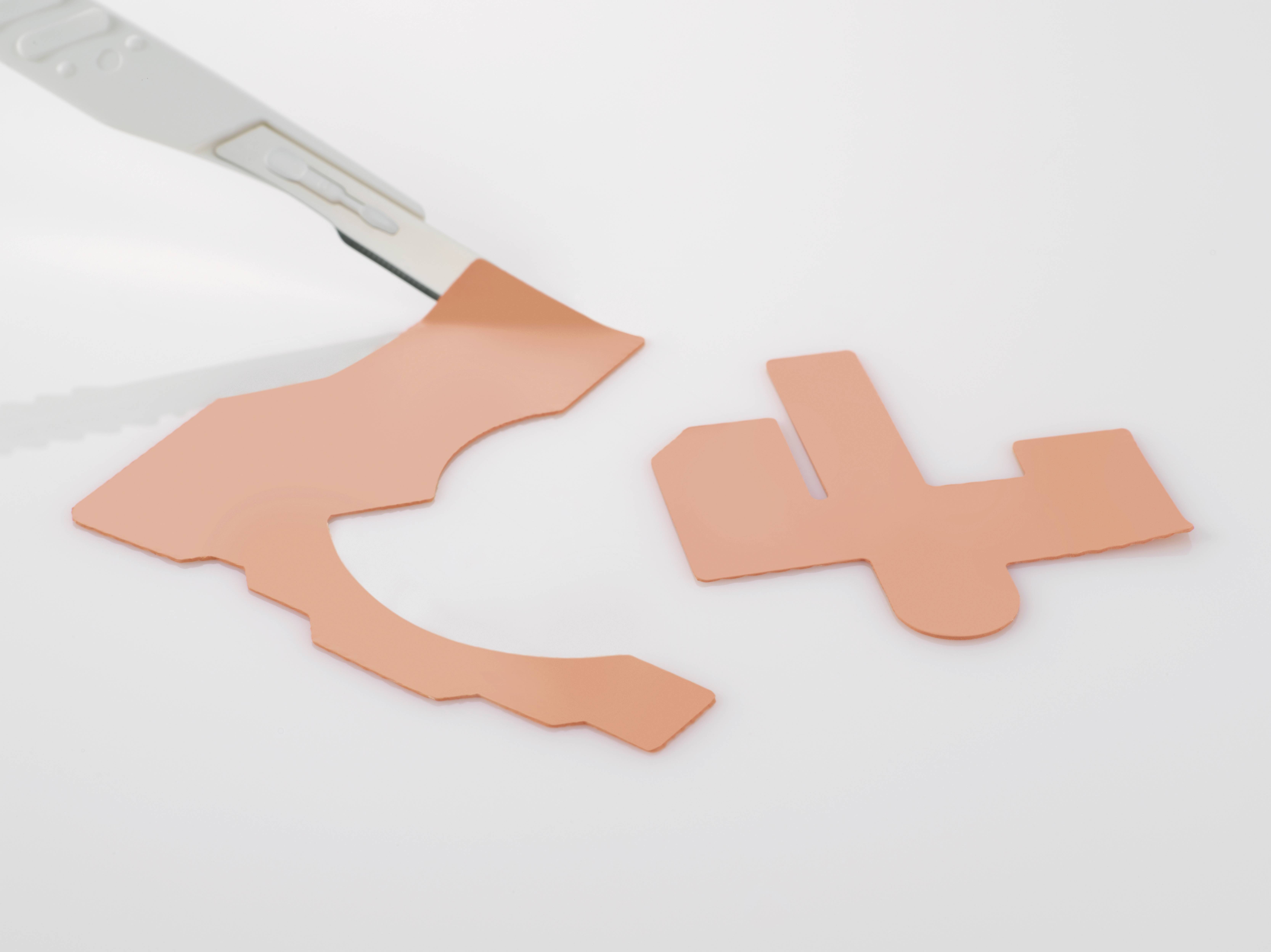 A copper moulding piece is cut out with a scalpel. Next to it, a cut-off piece lies on a white surface.