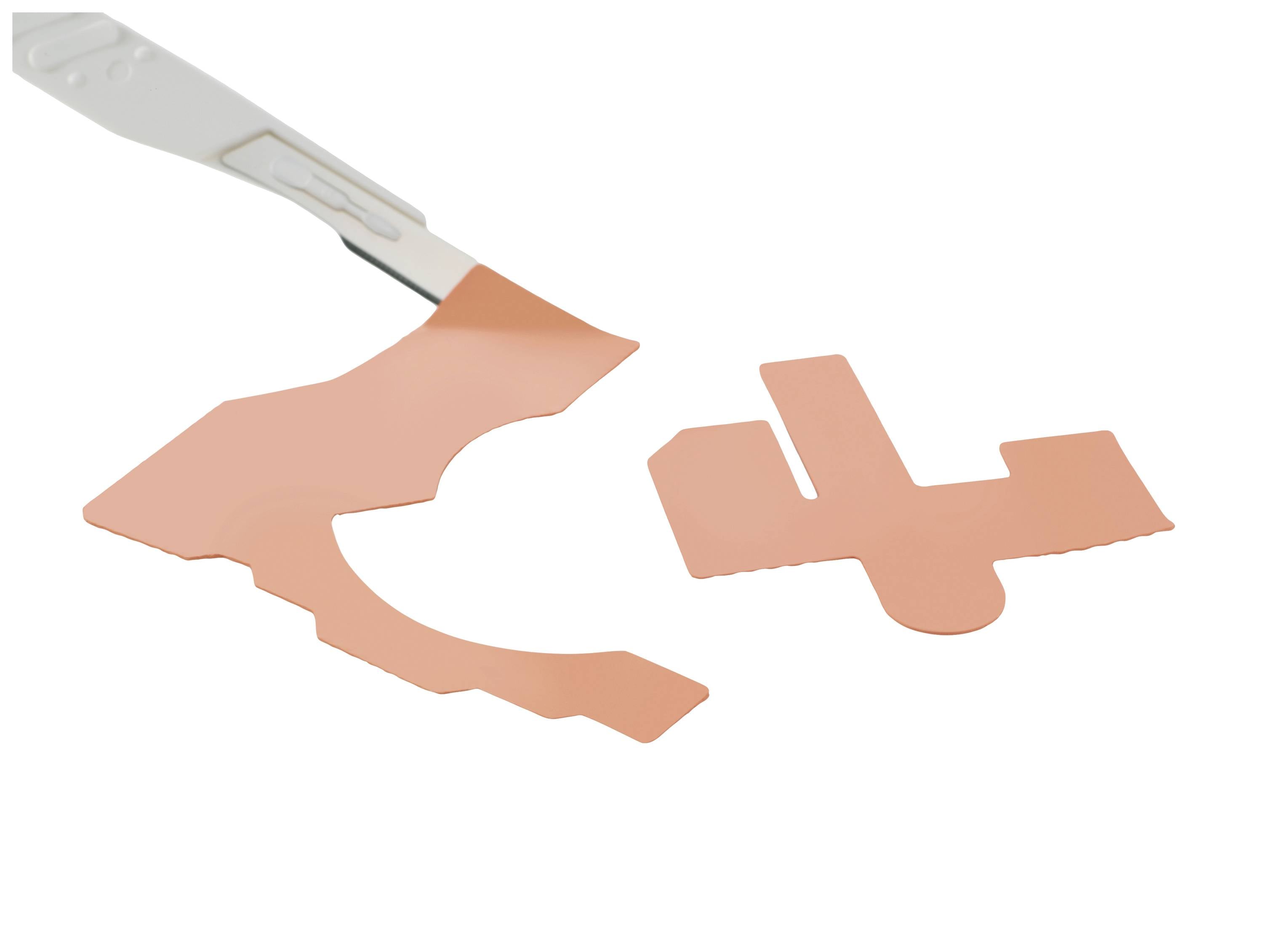 A cutting tool lifts pink material remnants beside a cut-out shape.