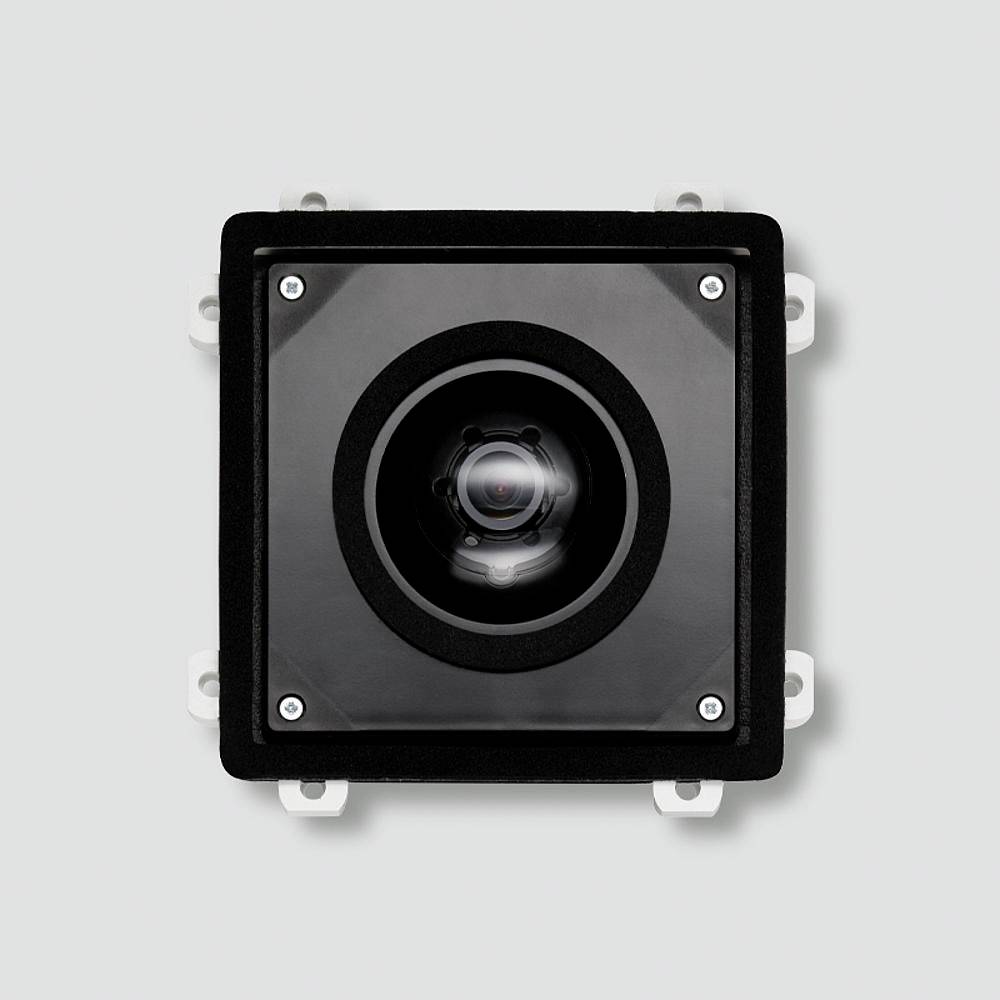 A square black camera with a centred lens and four screws at the corners, mounted on a grey surface.