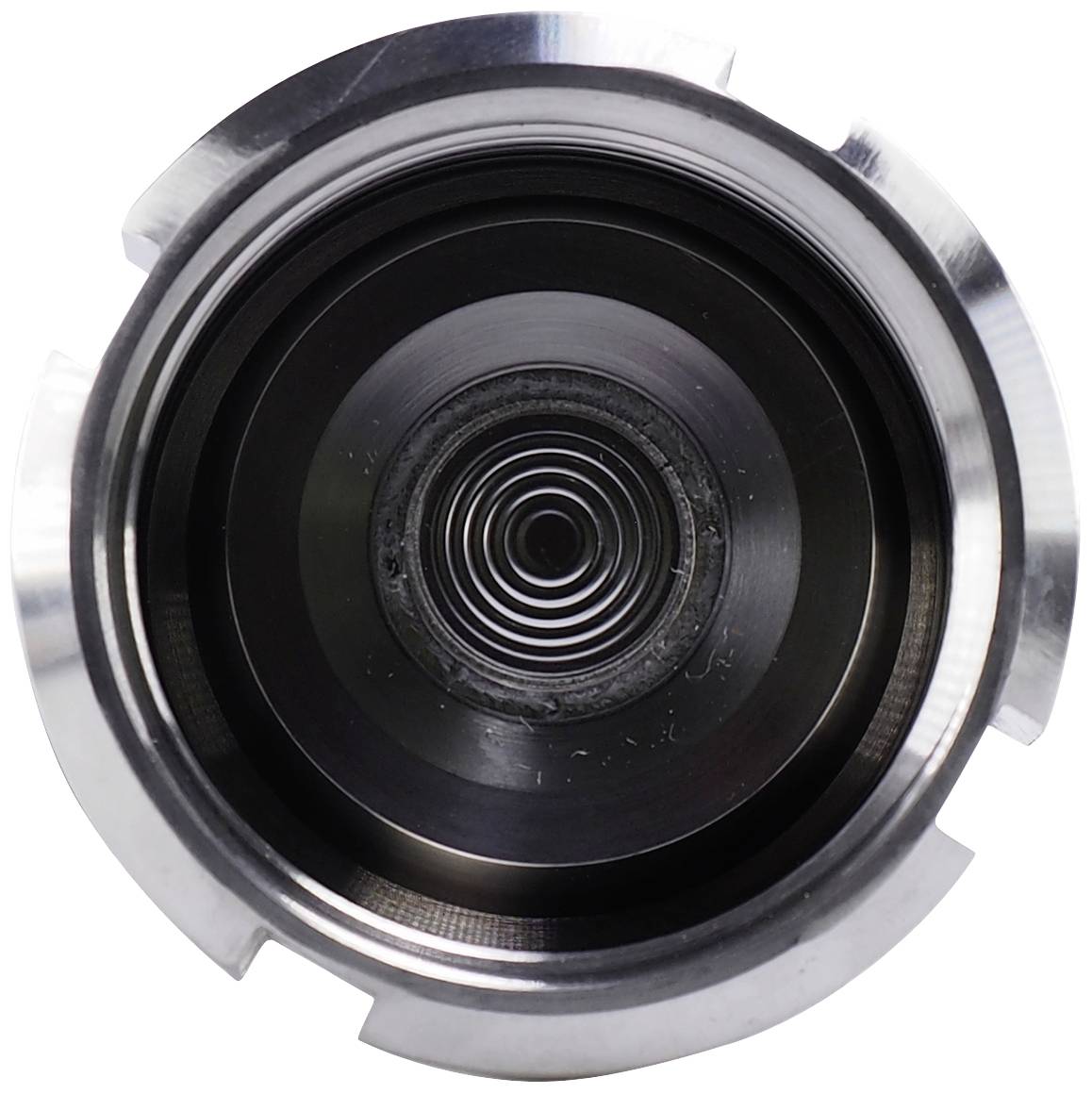 Circular metal structure with concentric rings, resembling a camera lens mechanism, with a central aperture at its centre.