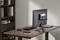 A modern desk with a monitor, keyboard, laptop, two notebooks and a mouse in an office with a bookshelf.