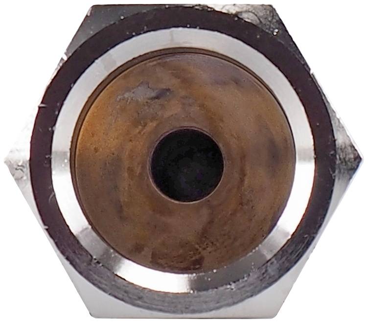 Close-up of a roasted metal nut with a hexagonal shape. The central opening shows signs of wear and oxidation.