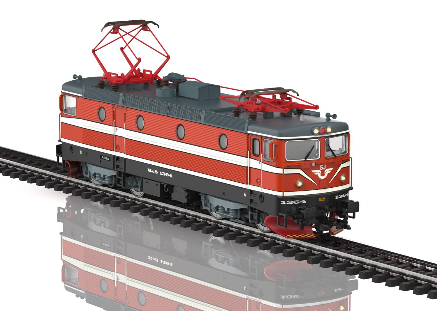 A red model railway locomotive on tracks, with electrical overhead power lines. The locomotive is standing on a reflective surface.