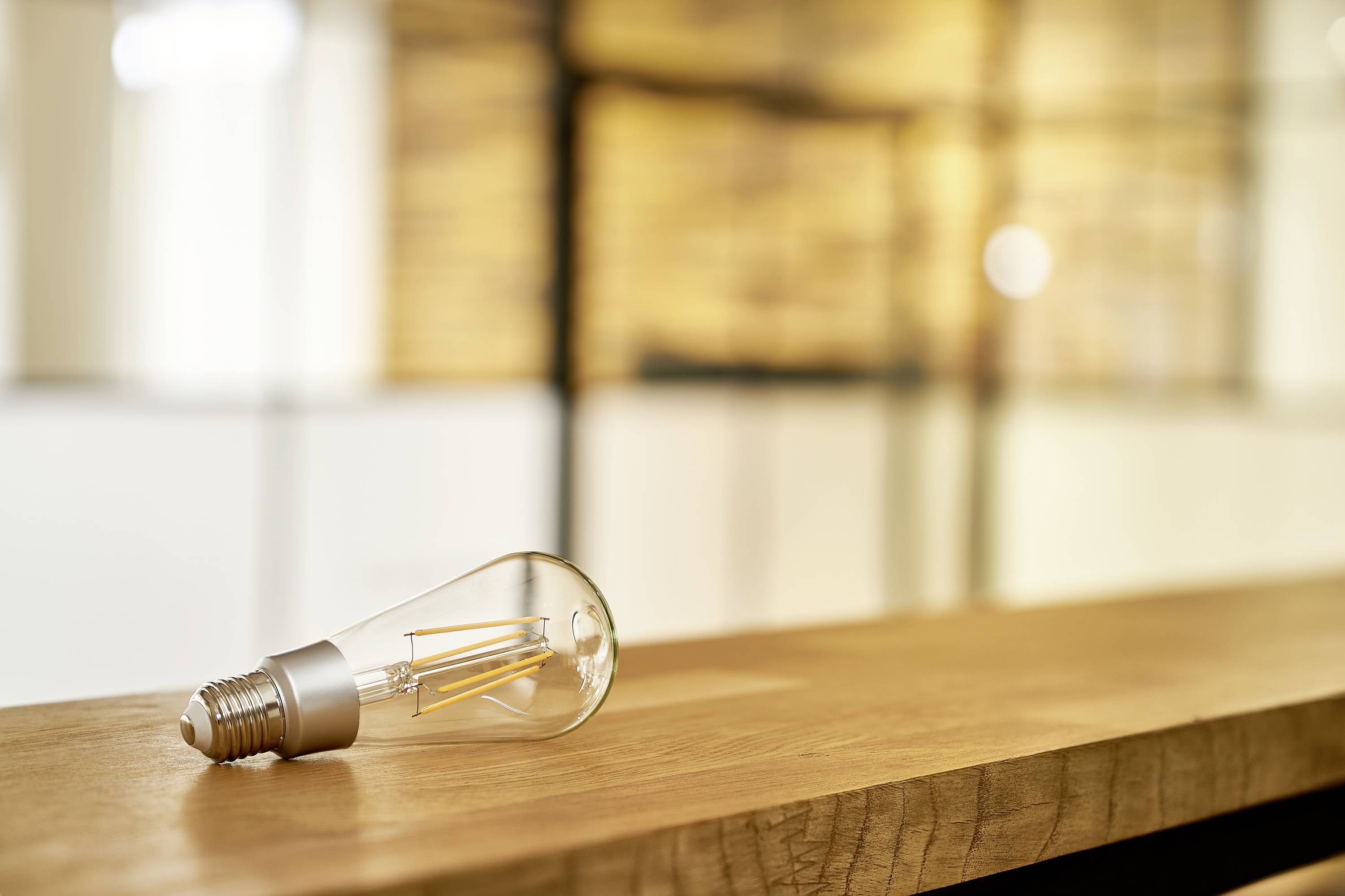 A light bulb rests on a wooden table, with a blurred background of warm light tones, symbolising ideas or energy.
