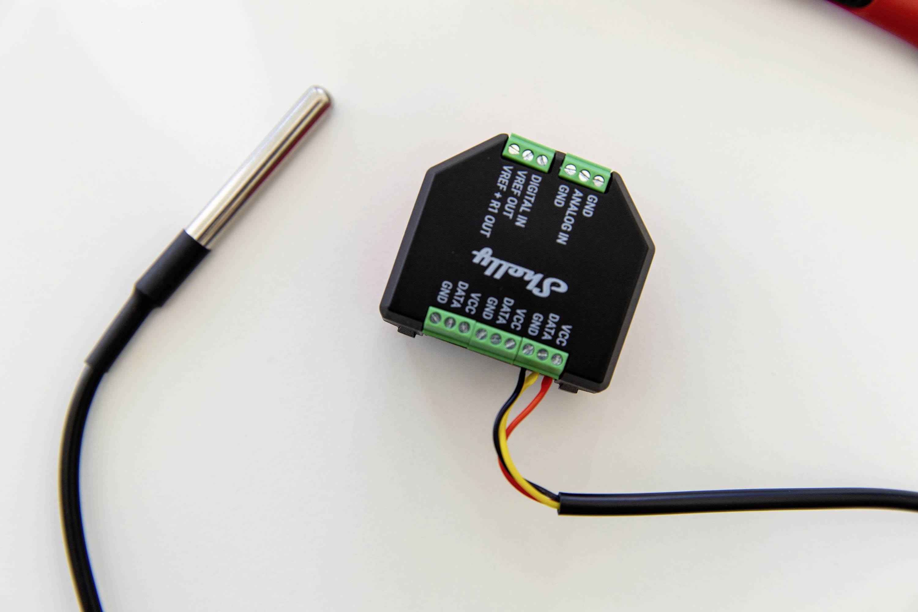 Electronic device with cables and connections on a white background. A metal pin, likely a sensor, is located on the left.