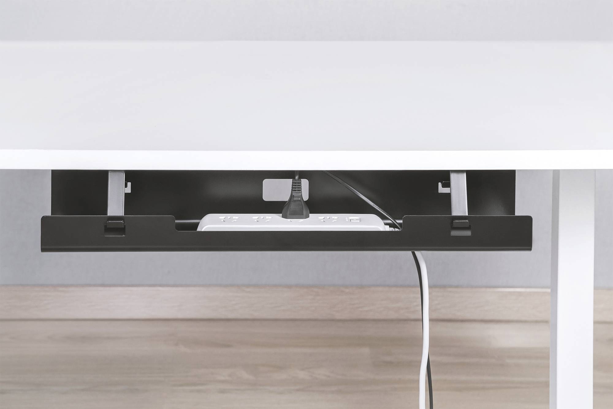 A white table with a black cable management solution underneath, neatly concealing cables and a power strip.