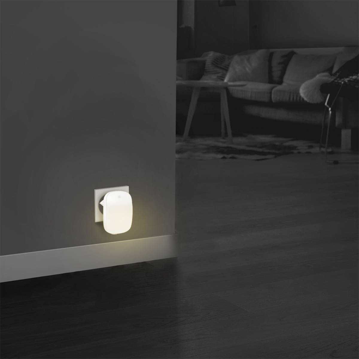 A night light illuminates a dark room, its light emanating from a socket near the floor. In the background, a sofa.