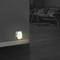 A night light illuminates a dark room, its light emanating from a socket near the floor. In the background, a sofa.