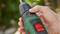 A hand is holding a green cordless screwdriver with red details. The screwdriver is set to a low torque setting.