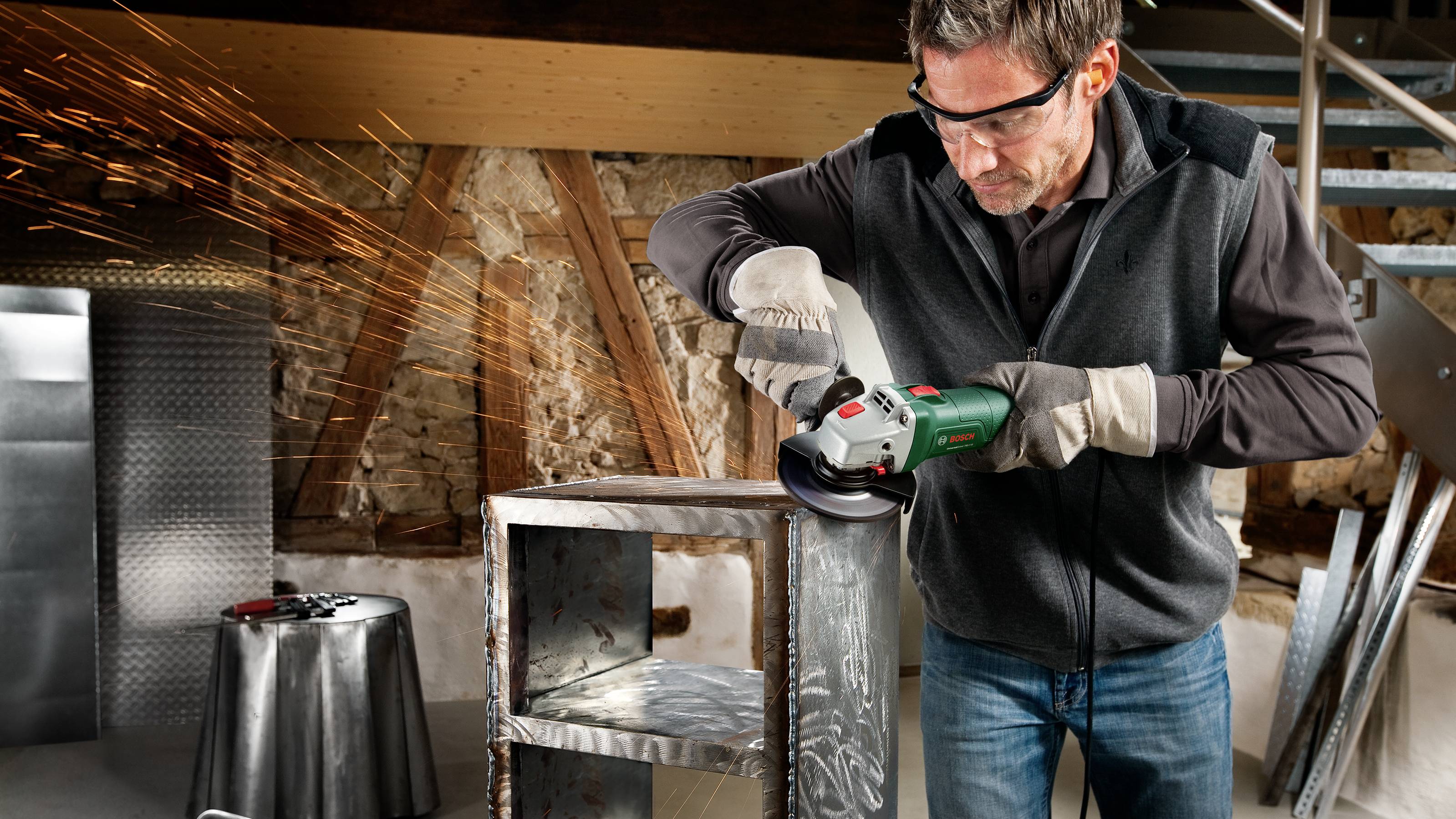 A man wearing safety glasses and gloves is using an angle grinder to create sparks while working on a metal object.