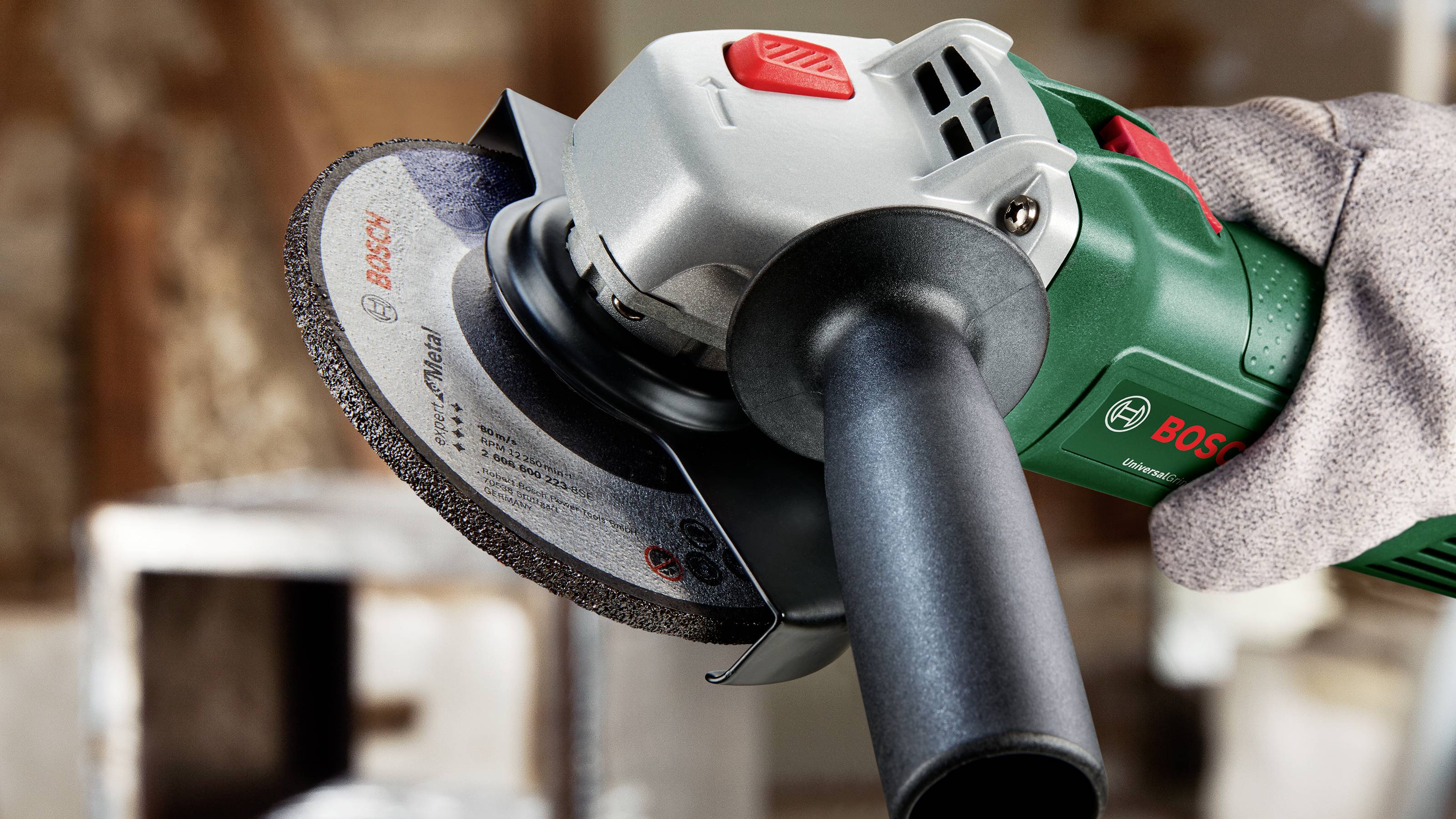 Close-up of a person holding a green angle grinder with a grey grinding disc. Focus on the tool.