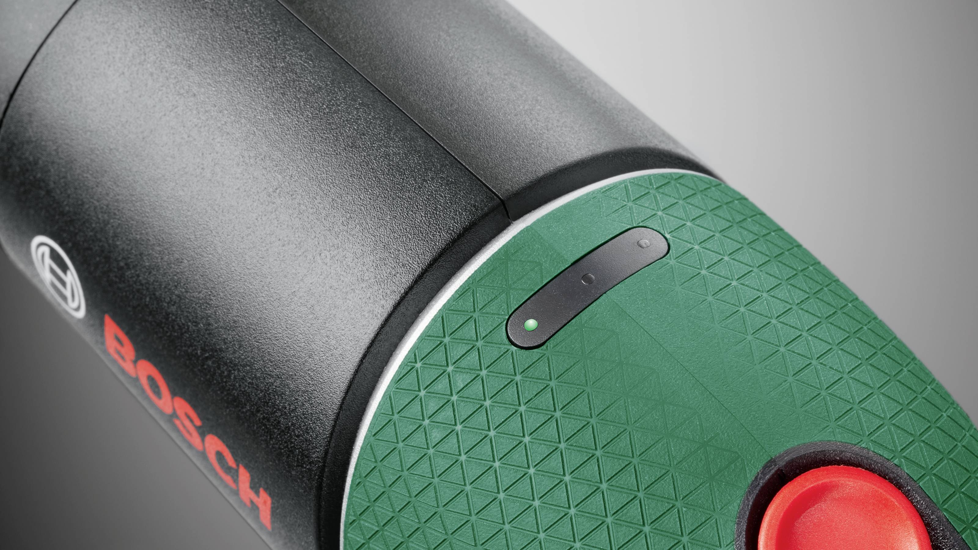 A section of a green electric tool with a black housing and Bosch logo. The focus is on a red release button and textured surface.