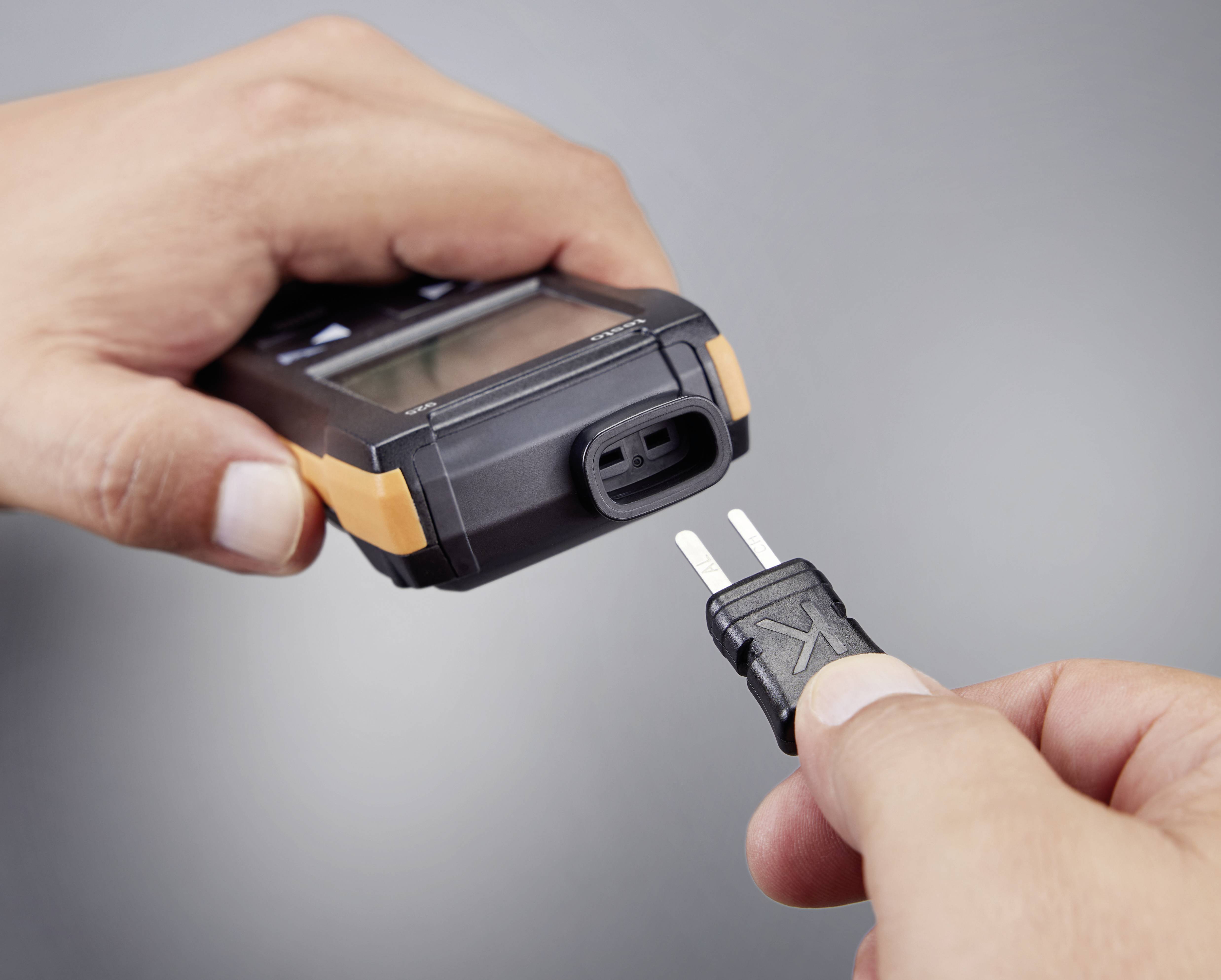 Two hands are showing a thermometer. One hand is holding the device, while the other is inserting the sensor plug into the thermometer.