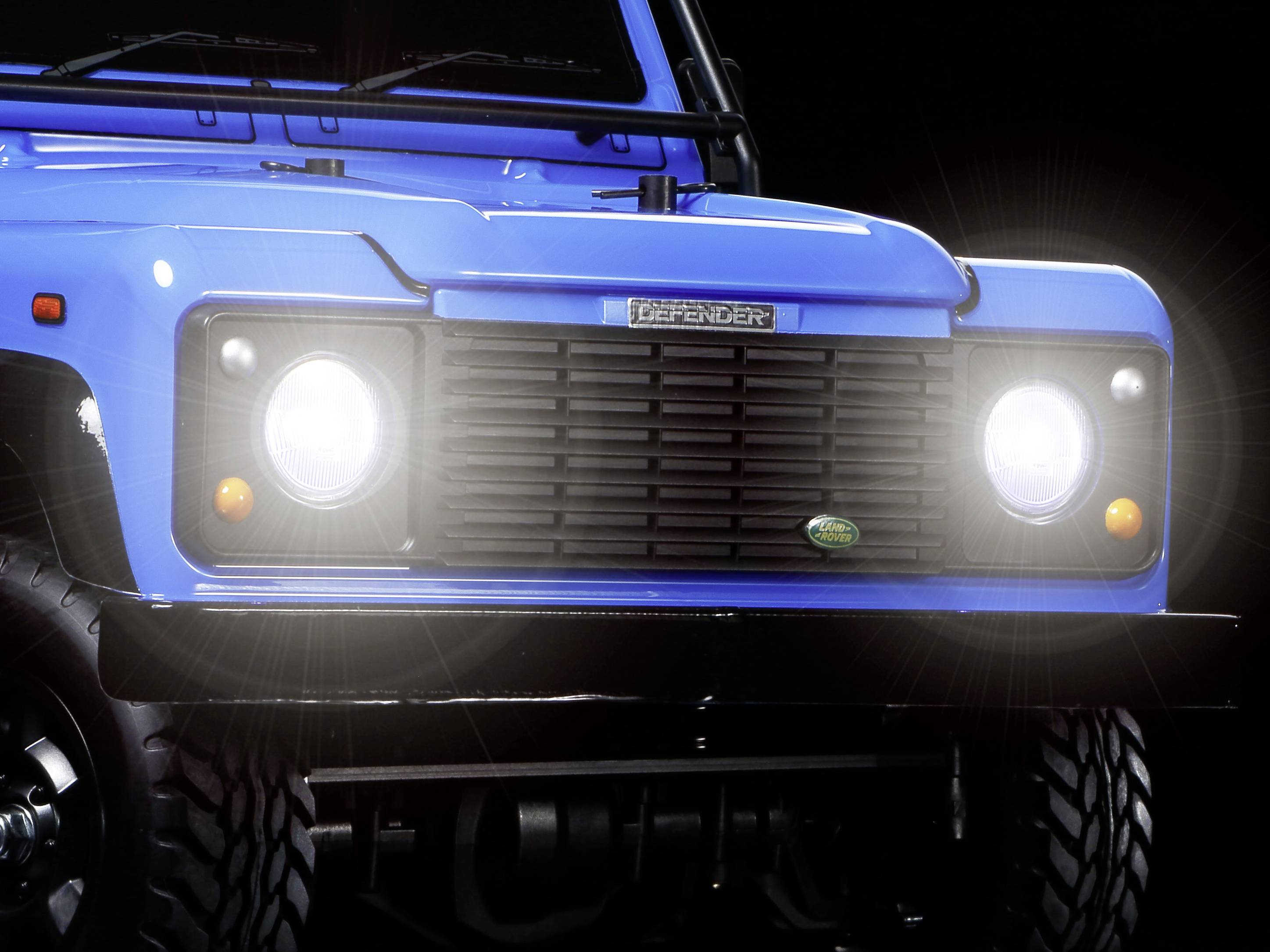 Front view of a blue SUV with headlights on in a dark environment.