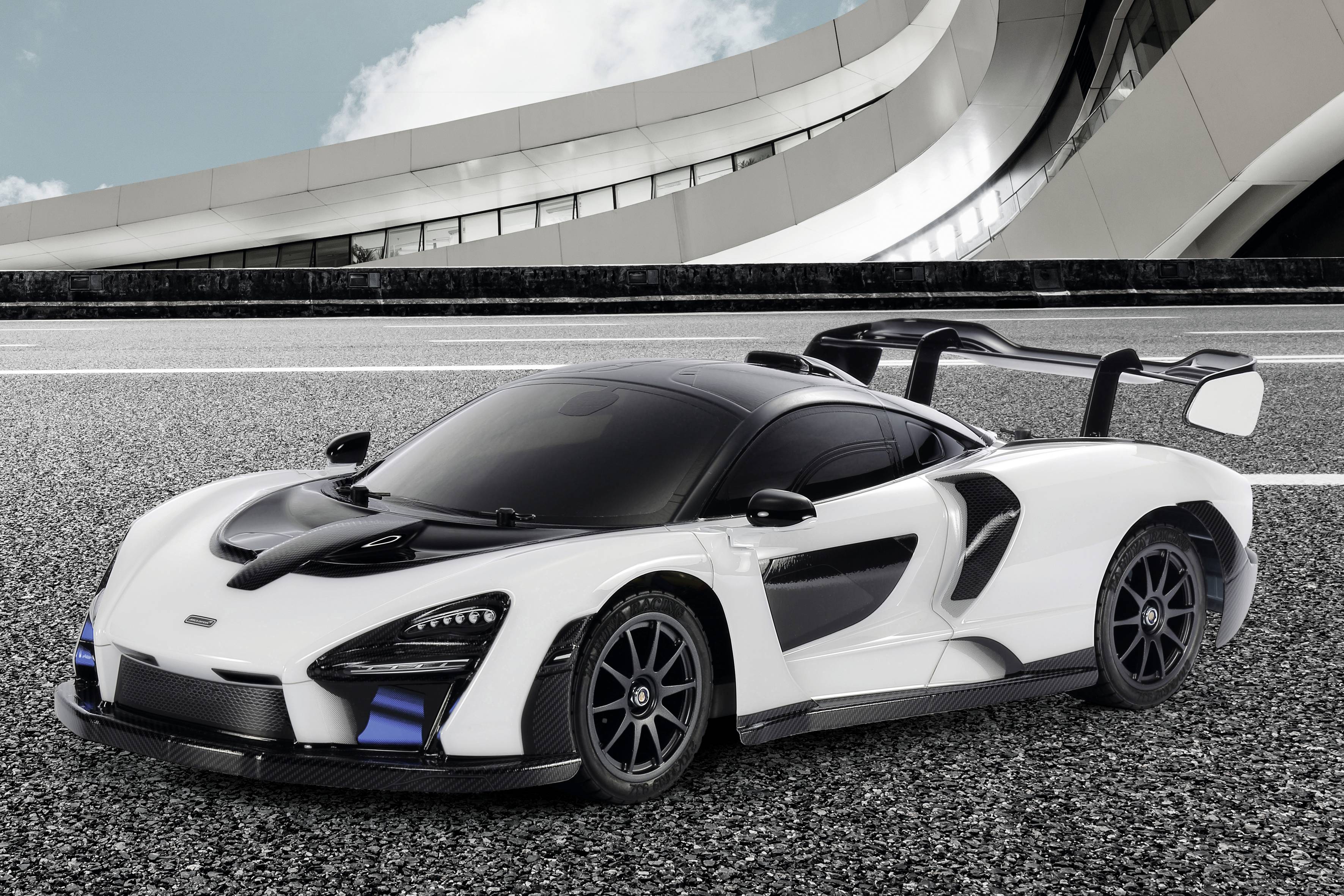 A white supercar with black details is parked on a road in front of a modern, curved building.