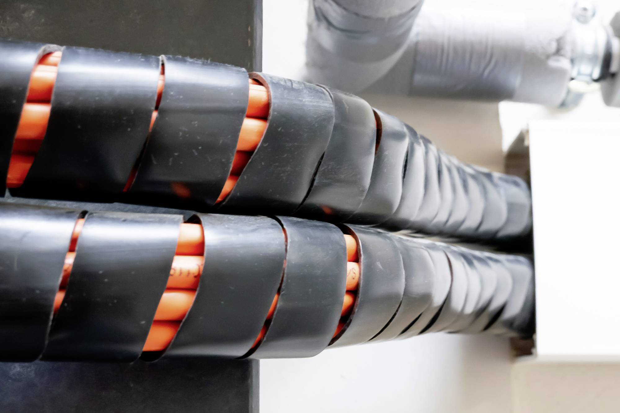Two thick cable bundles with black outer sheaths and orange elements run parallel along a light-coloured wall.
