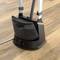 A steam cleaner is standing on a wooden floor. It has a black, curved water reservoir and a rotary switch at the base.