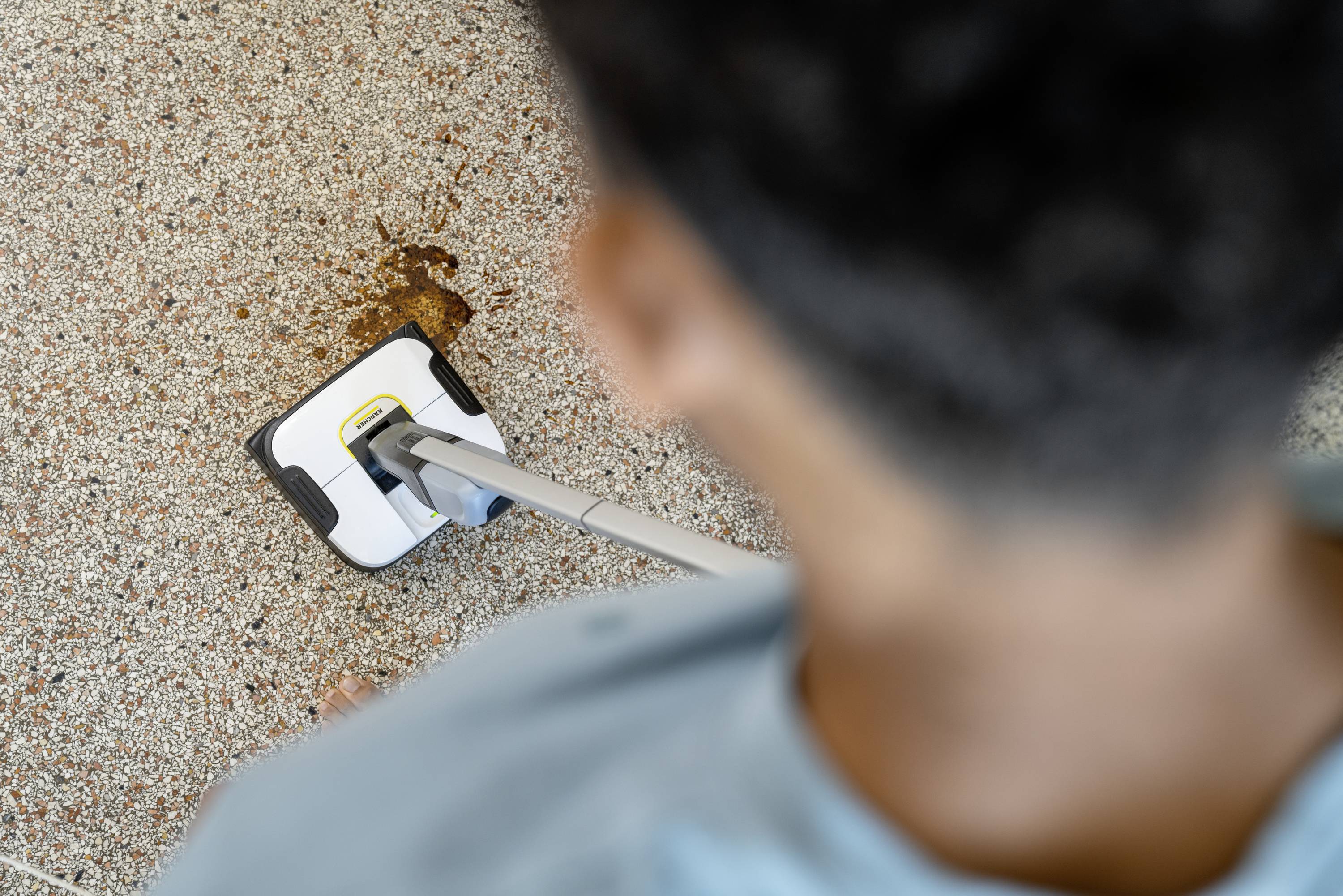 A person is cleaning a dirty mark on a tiled floor with a mop.