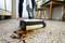 A floor cleaner is vacuuming spilt liquid from a terrazzo floor. In the background, a person is standing beside a table.
