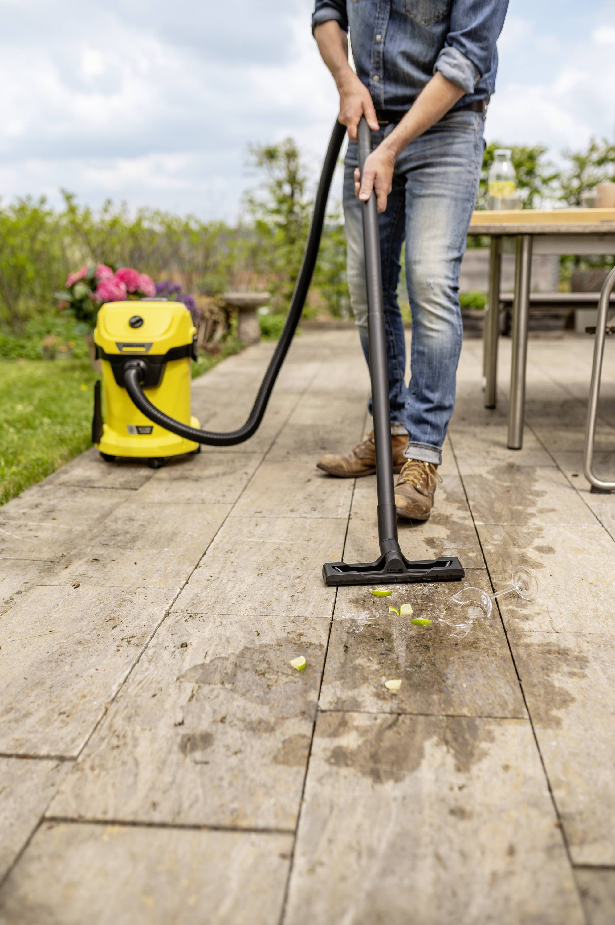 A person is cleaning a wooden decking with a yellow wet and dry vacuum cleaner. Dirt and water are present on the floor.