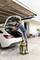 A man in casual clothing is vacuuming the boot of a white car in a garage. Next to him stands a yellow vacuum cleaner.